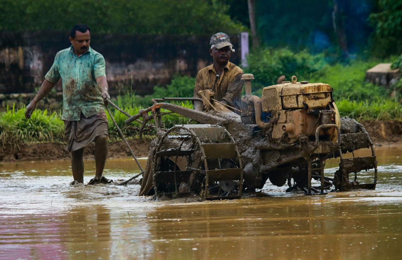 Two farmers working a flooded paddy field with a mud-covered power tiller