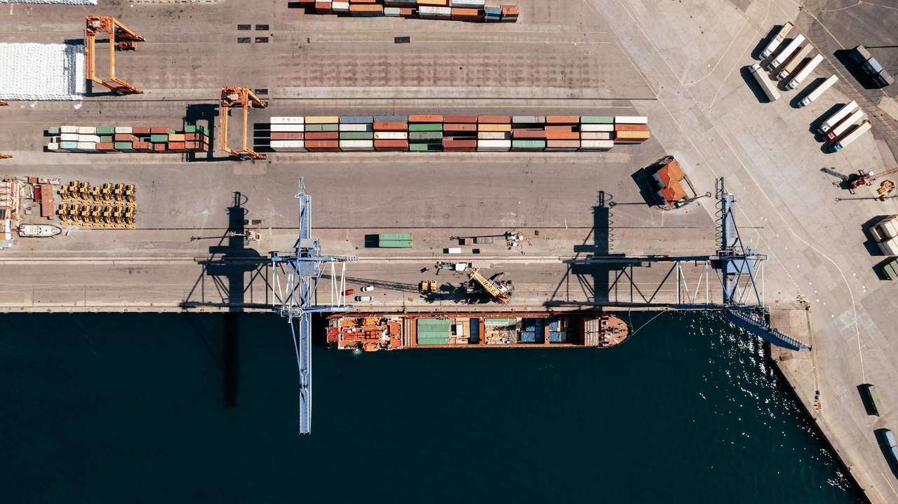 Aerial view of a cargo ship moored at a port quay beside cranes and stacked containers