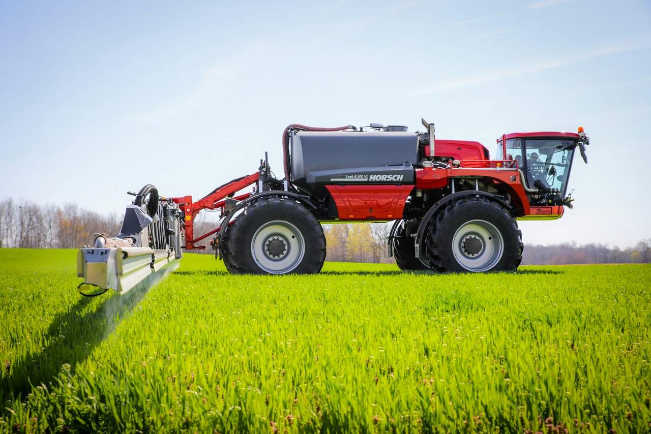 A red self-propelled crop sprayer working in a green field under a blue sky