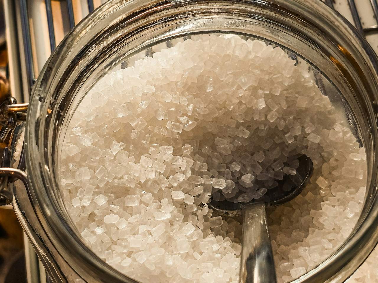 Close-up of coarse white sugar crystals in a glass jar with a metal spoon