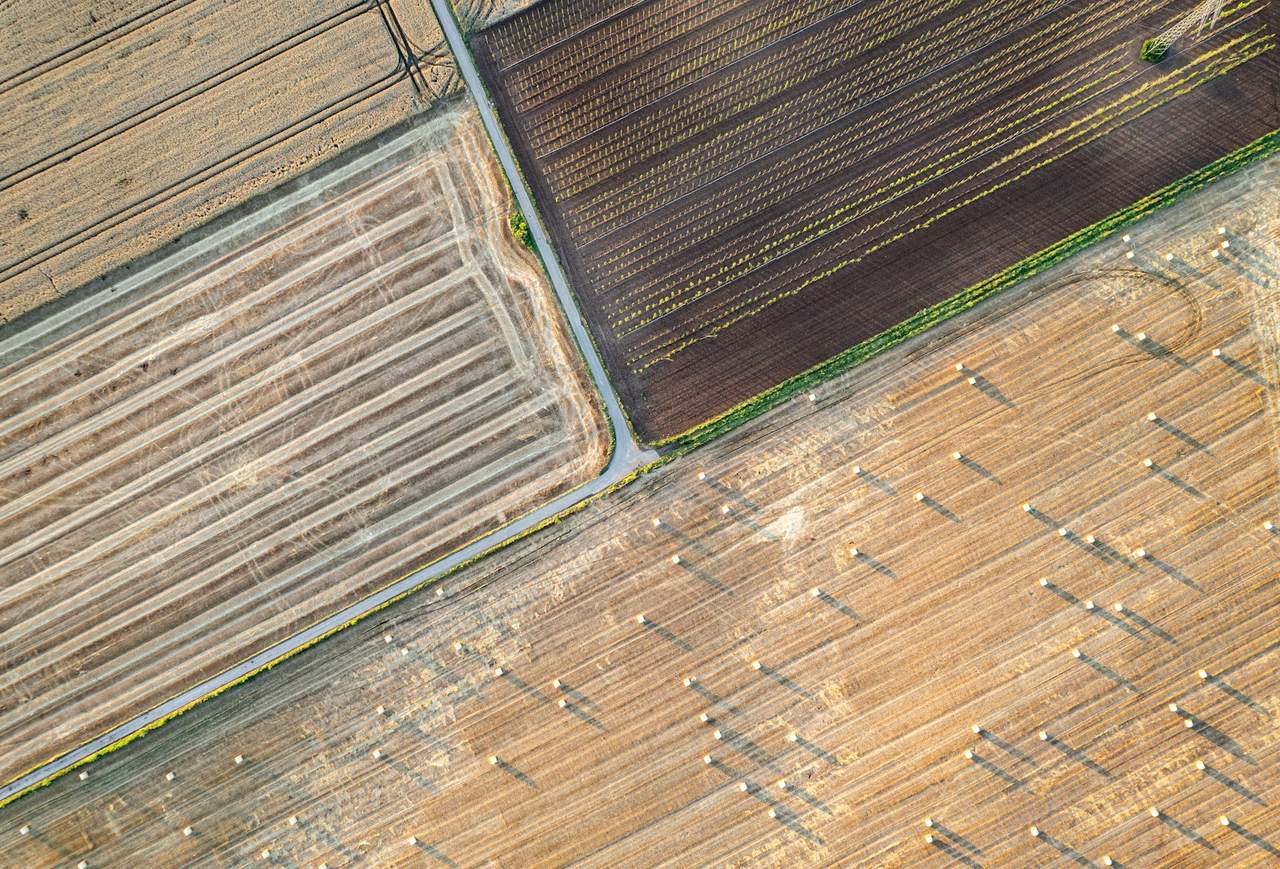 Farmland seen from above, with harvested rows, planted fields and hay bales
