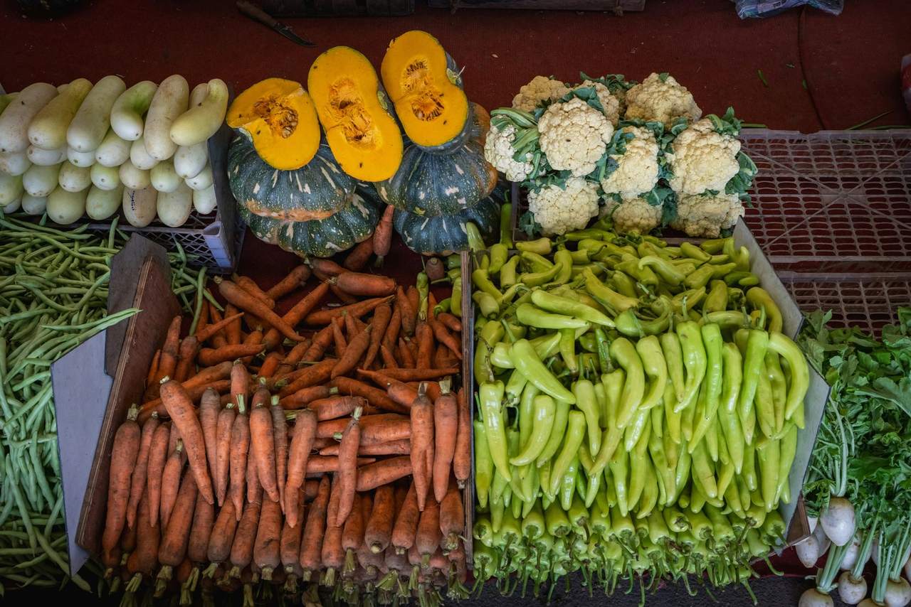 Crates of carrots, green peppers, cut pumpkins, cauliflowers, beans and gourds on a market stall