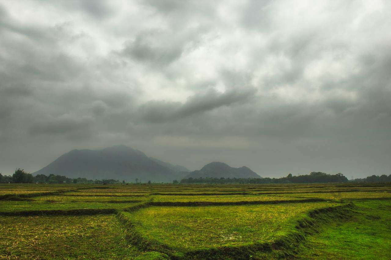 Heavy grey clouds over flat green fields with hills on the horizon
