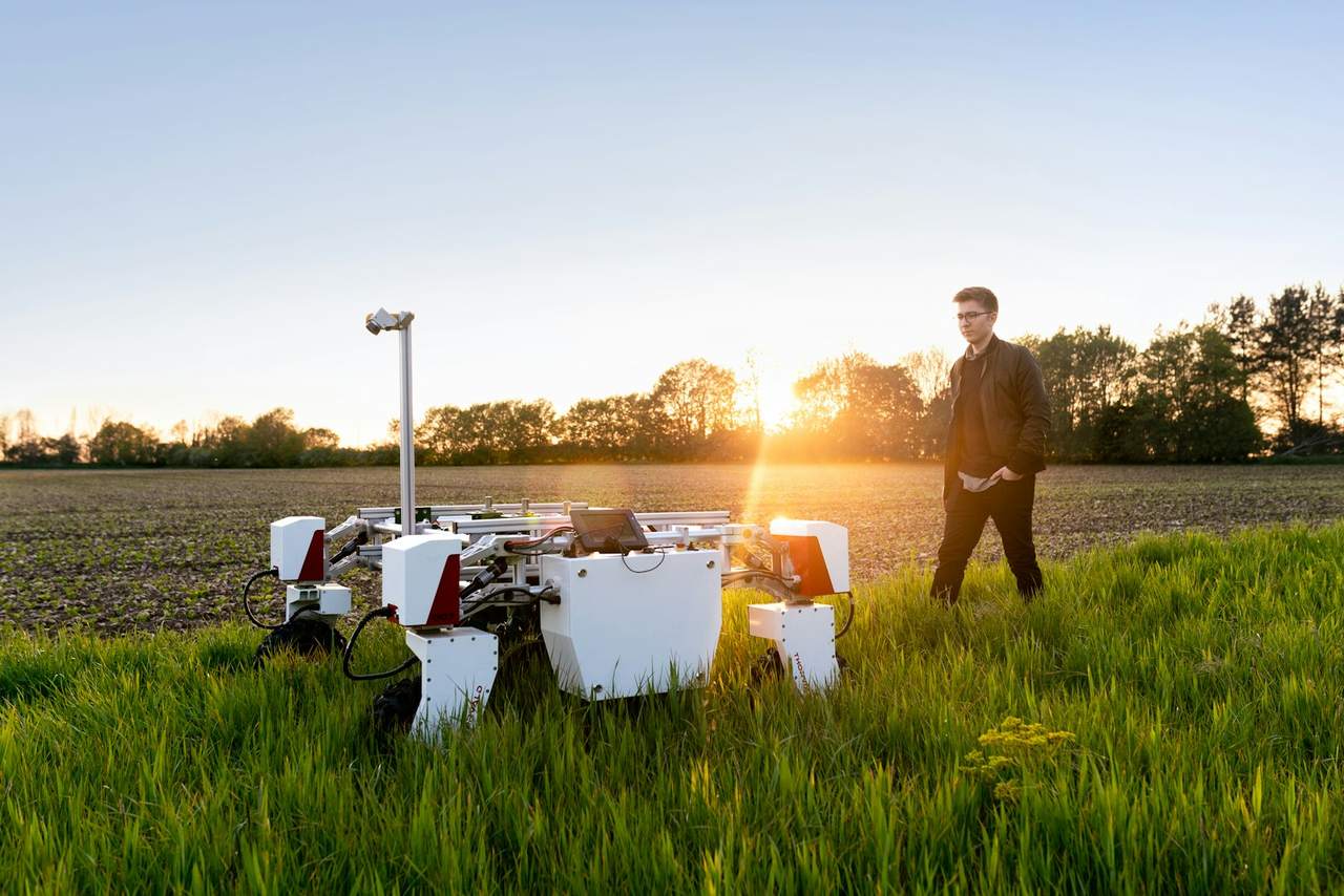 A wheeled field robot on grassland at sunset, with an engineer standing nearby
